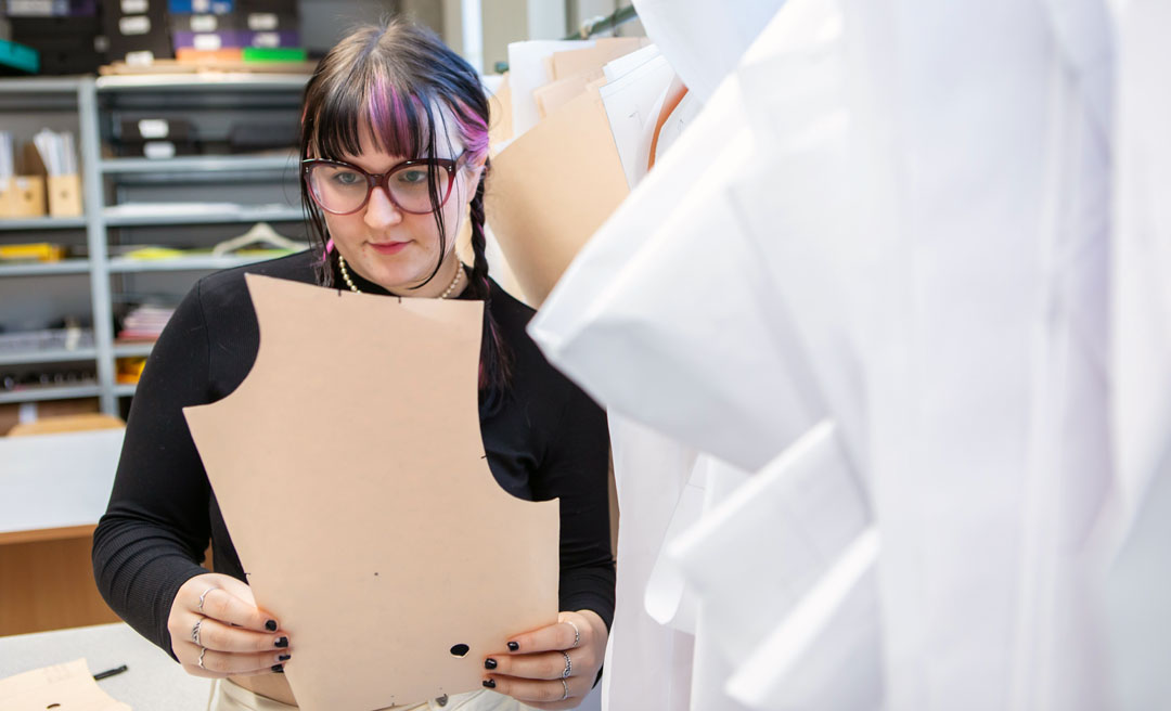 A fashion student examining a paper pattern for garment design in a sewing studio.