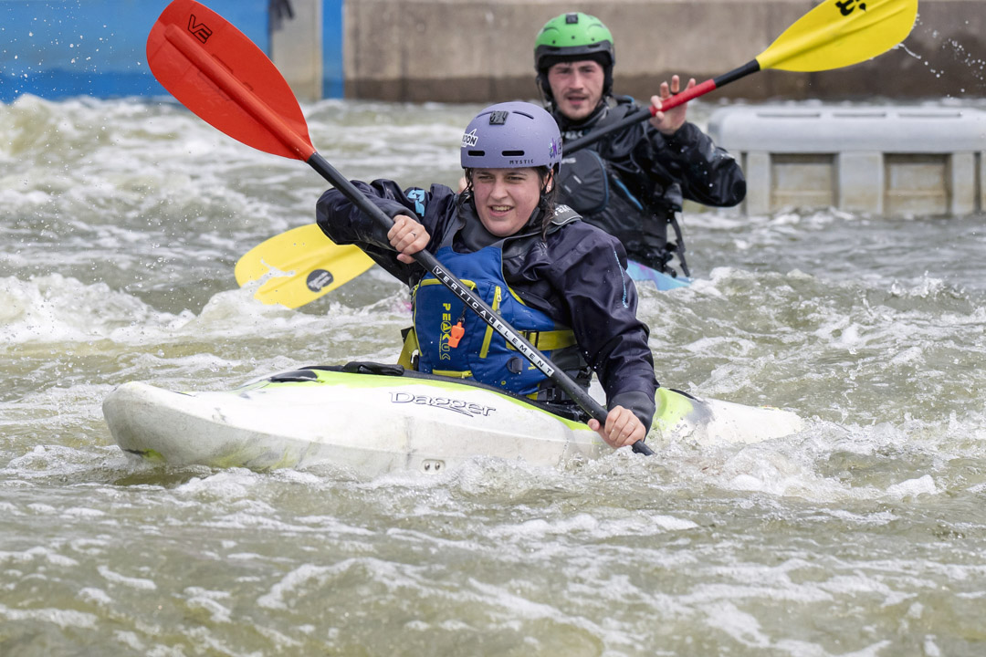 Two people kayaking in whitewater rapids, wearing helmets and waterproof gear during an outdoor activity session.