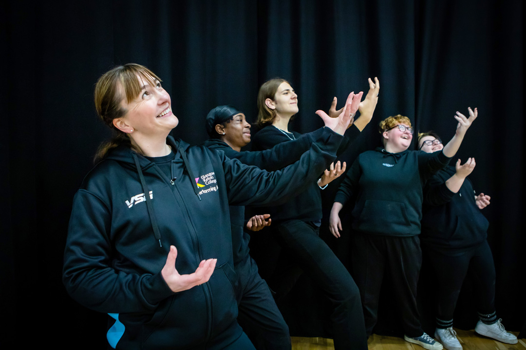 Performing arts lecturer leading a drama exercise with students, demonstrating expressive hand and body movements.