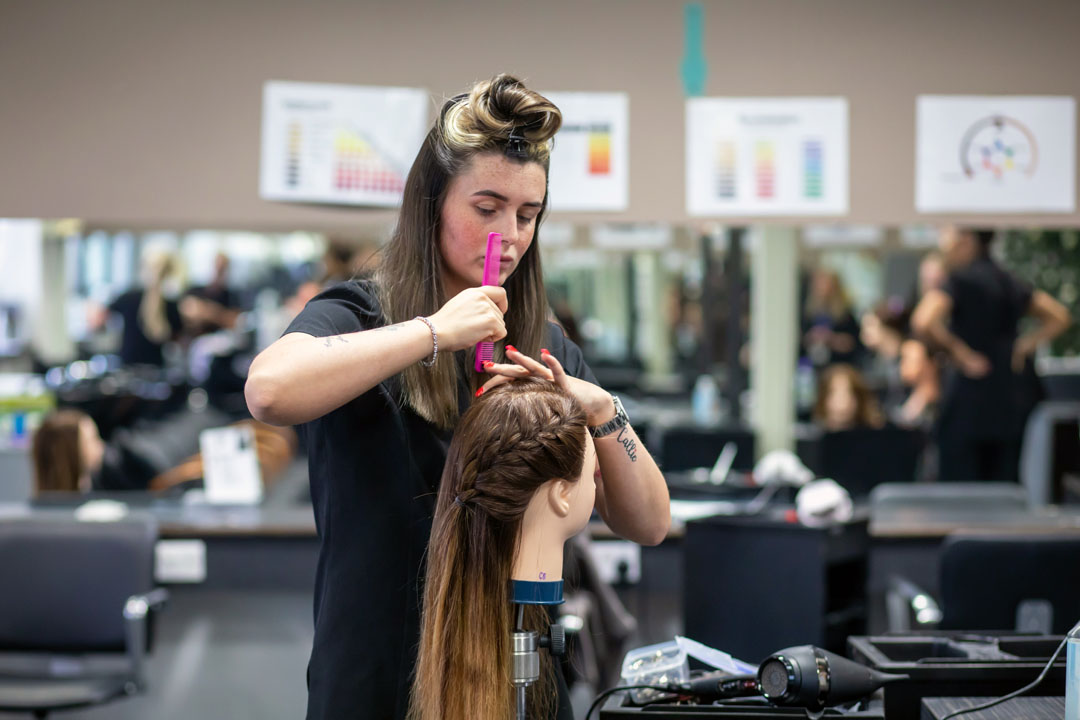 Hairstyling student carefully styling a mannequin’s hair in a salon.