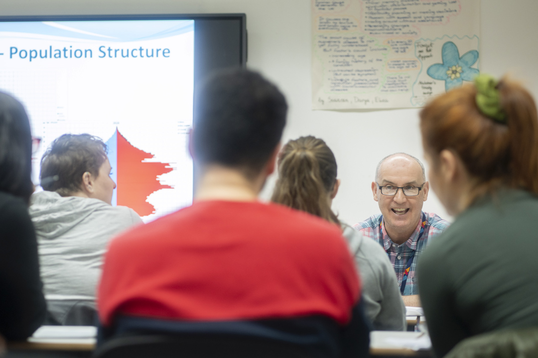 Lecturer smiling while teaching population structure in a lively classroom discussion.