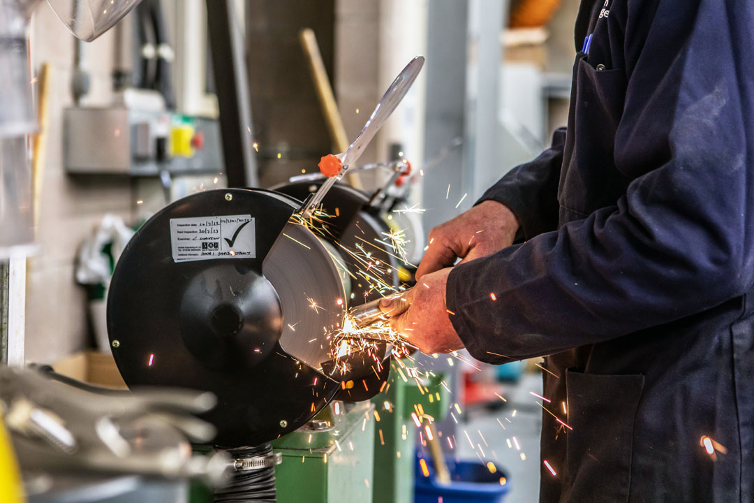 Close-up of a grinding wheel in action, with sparks flying as a lecturer in a navy-blue coat sharpens a metal component.