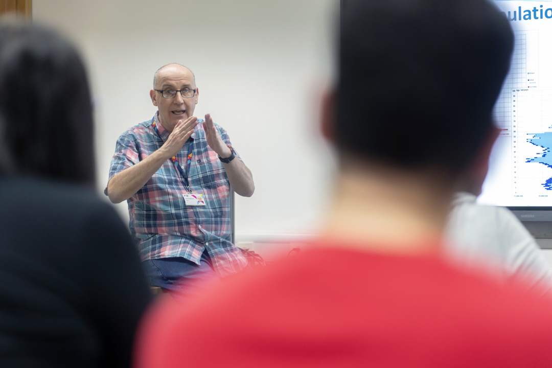 Lecturer uses hand gestures while explaining a topic to students in a humanities lesson.