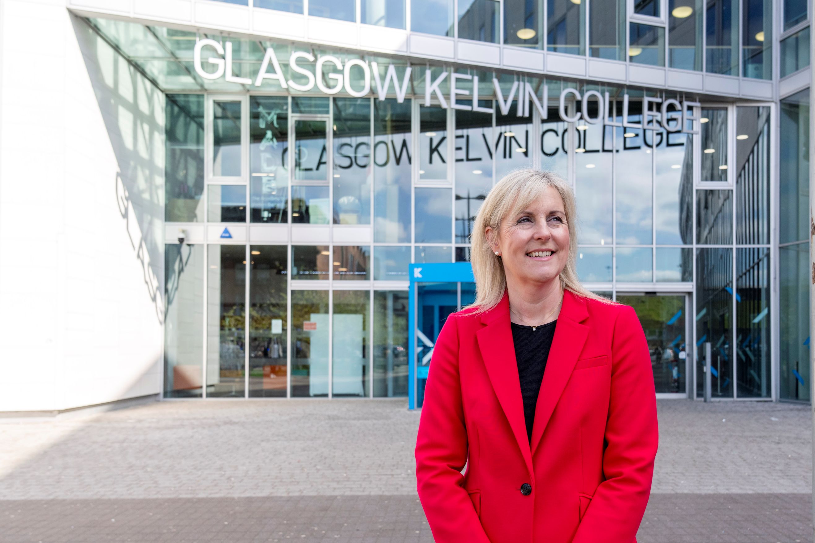 Joanna Campbell, Principal of Glasgow Kelvin College, smiling outside the college’s main entrance in a bright red blazer