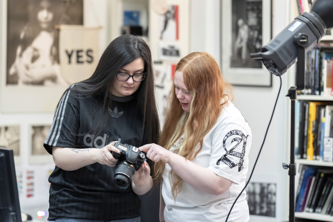 Two students reviewing photos on a DSLR camera in a creative photography studio.