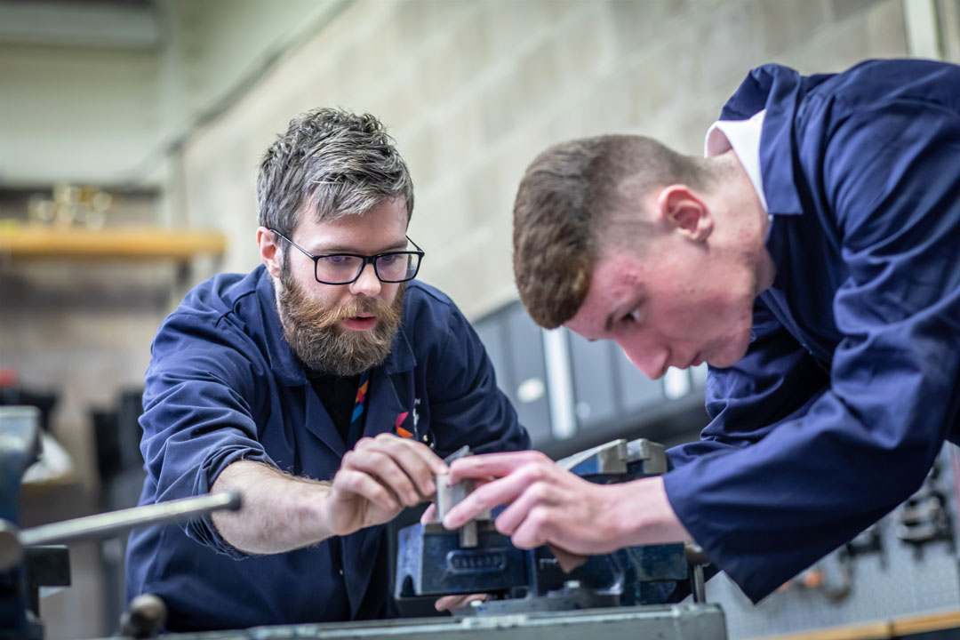 Lecturer and student working together on precision metalwork using workshop equipment.
