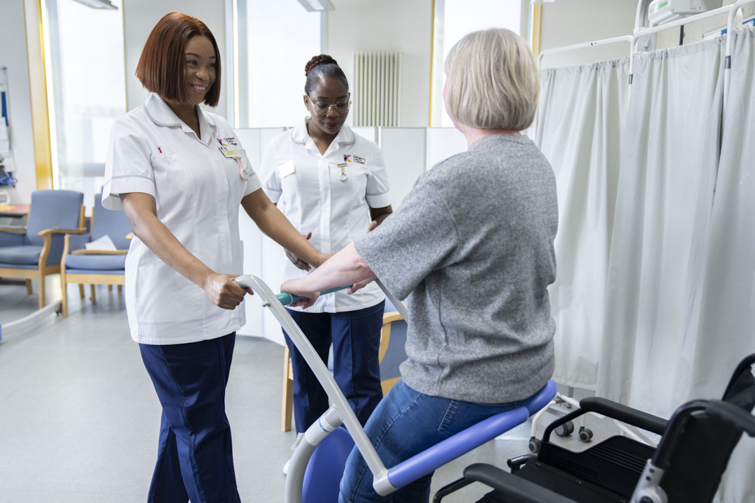 Two healthcare students assist a patient using a mobility aid in a simulated care environment.