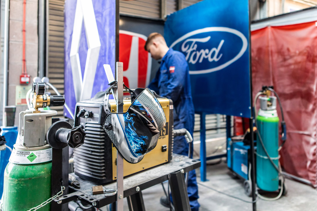 Close-up of automotive welding area showing gas cylinders and a protective welding mask.