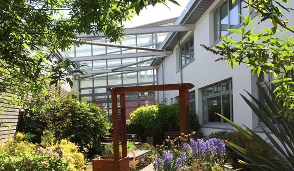 Lush garden courtyard at John Wheatley College featuring flowers, shrubs, and a wooden pergola under a glass canopy.