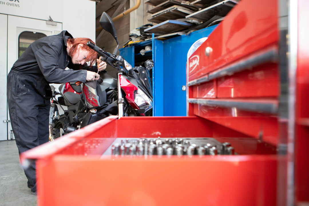 Student repairing a motorcycle beside a red tool chest in the automotive workshop.