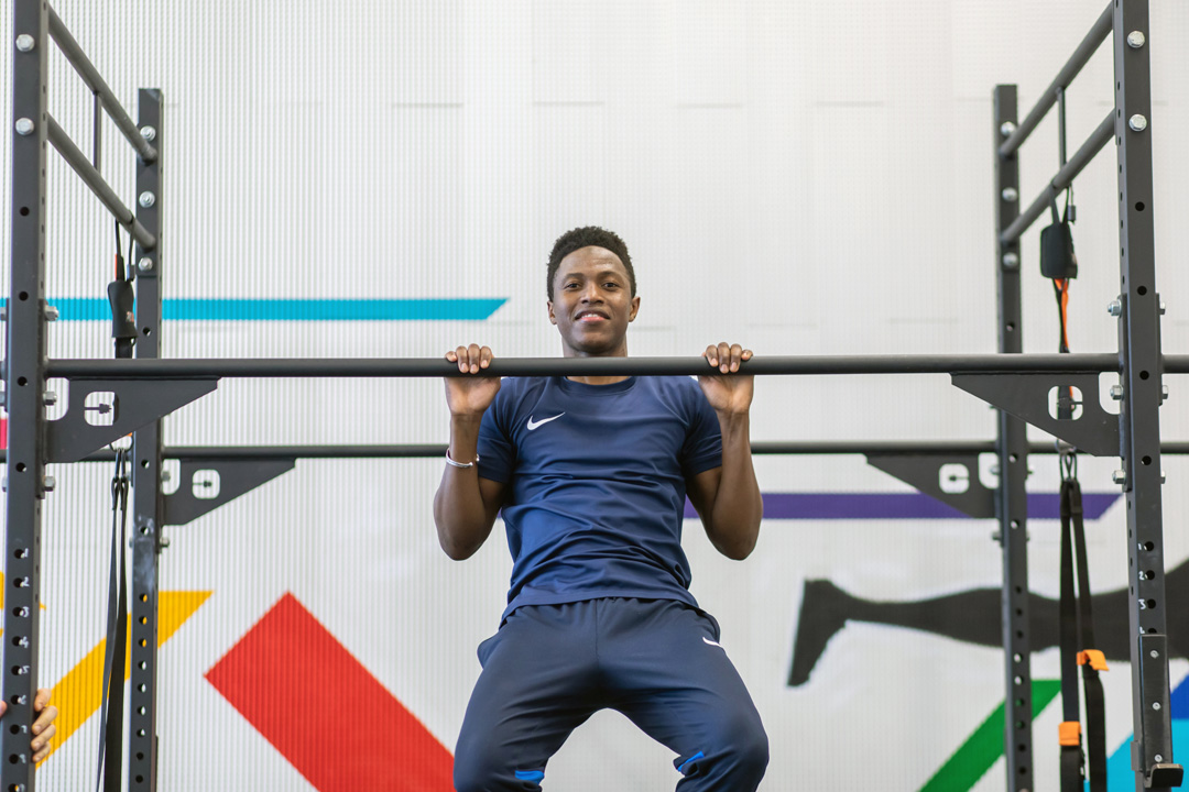 Student mid-pull-up on gym rig with colourful wall graphics behind.