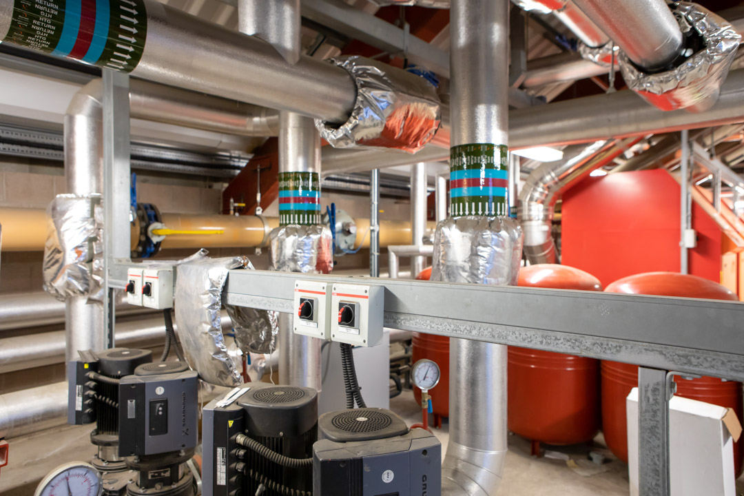 Close-up of interconnected heating system pipes, pumps, and insulated valves used for industrial heating and ventilation.