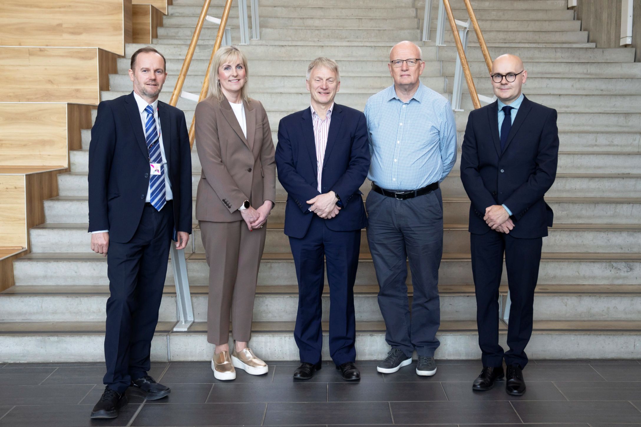 Five professionally dressed individuals standing on indoor stairs at Glasgow Kelvin College.