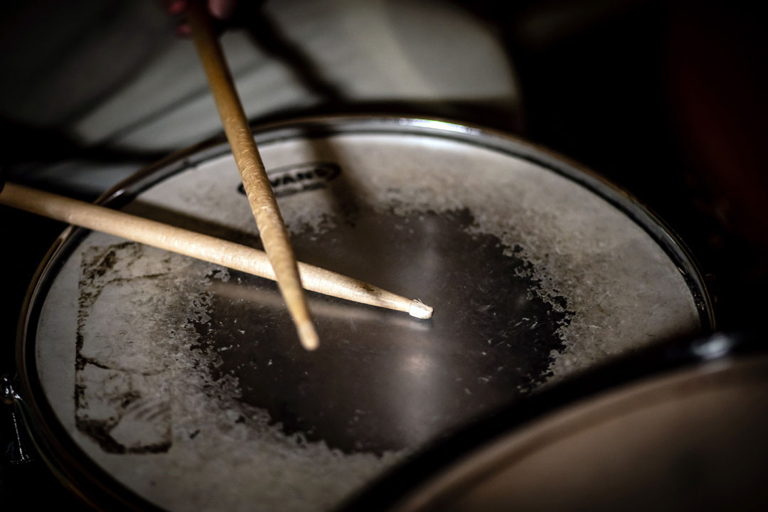 A pair of wooden drumsticks resting on a worn snare drum surface, showing signs of frequent use.