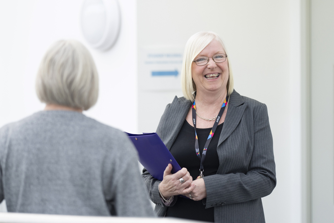 Pauline from Glasgow Kelvin College’s Finance team smiling and holding a folder while speaking with a colleague in a bright office space