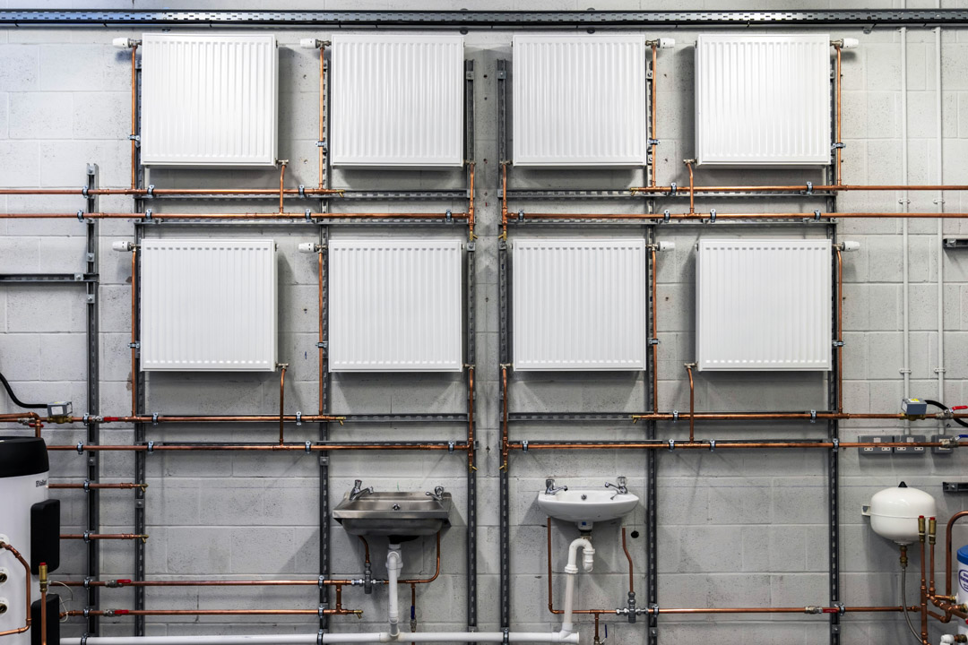 Wall-mounted radiators, sinks, and copper pipework arranged in a plumbing training workshop at Glasgow Kelvin College