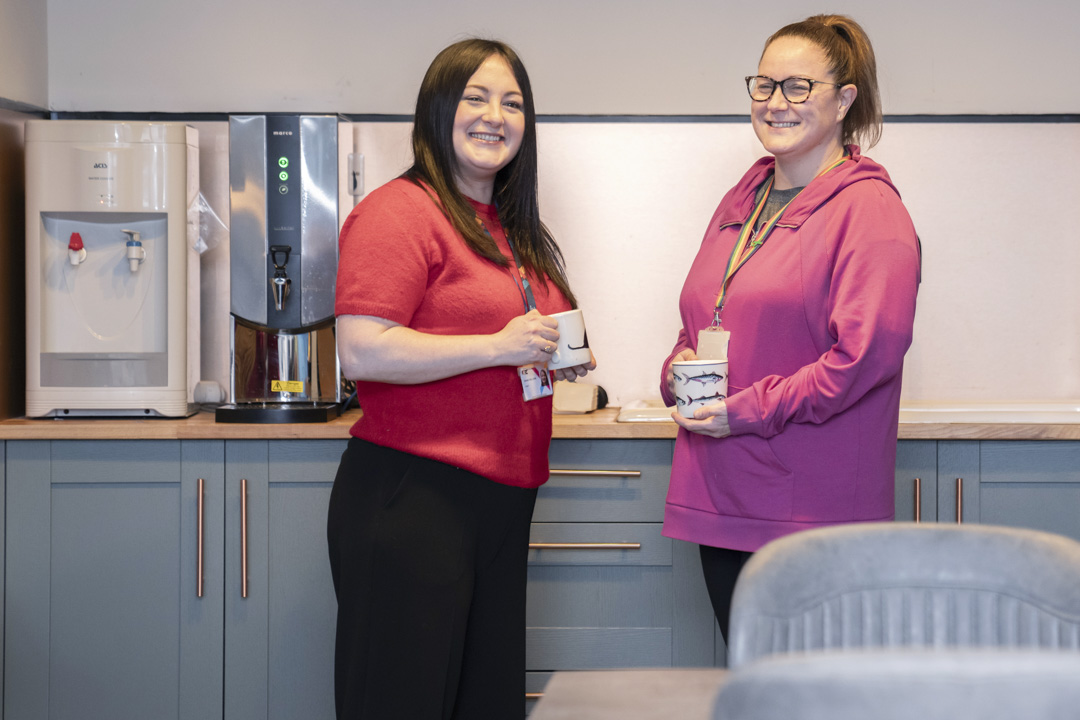 Two Glasgow Kelvin College staff members smiling and chatting over mugs in a staff kitchen area