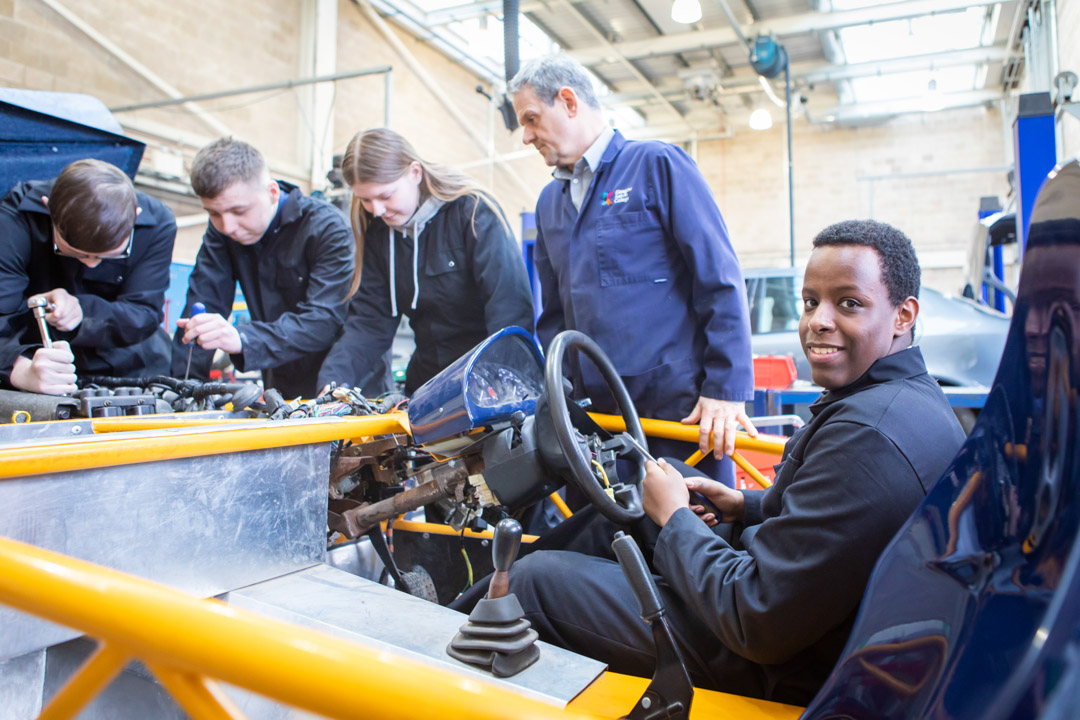 Instructor and students collaborating on an engine repair project, focusing on mechanical details in a hands-on learning session.