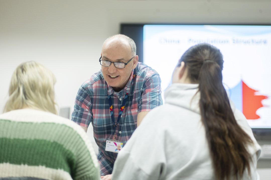 Smiling lecturer interacts closely with two students during a class at Glasgow Kelvin College.