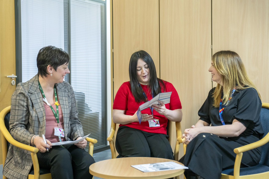 Three Glasgow Kelvin College staff members sitting together in discussion, with one holding a leaflet, in an office setting.