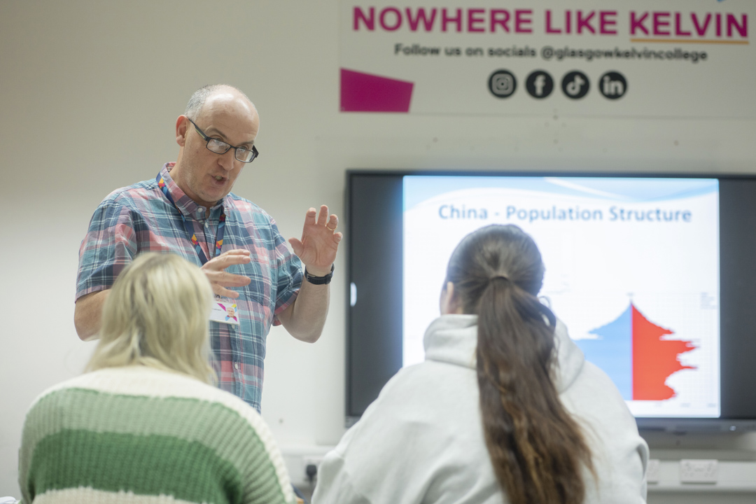 Lecturer speaks to students during a session on population structure, under a “Nowhere Like Kelvin” sign.