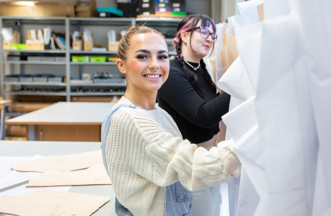 Two fashion students organizing and selecting design patterns in a creative workspace.