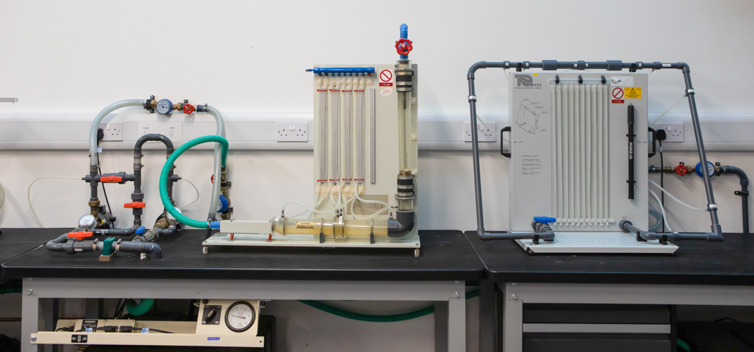 A set of fluid mechanics training rigs with interconnected pipes, valves, and flow meters, used for hands-on learning in a building services workshop.