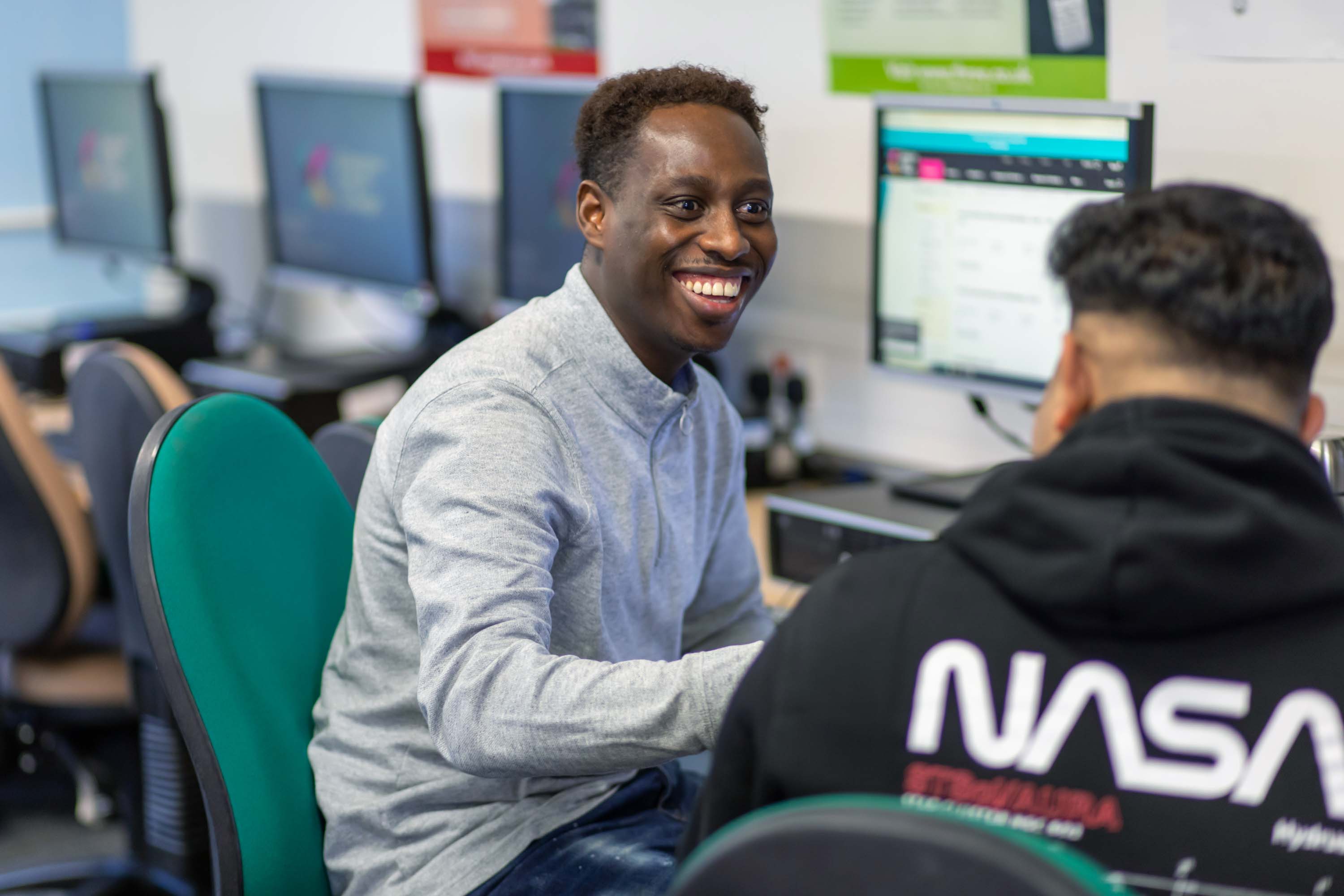 Two students working together at a computer in a business and administration course, one smiling while engaged in discussion.