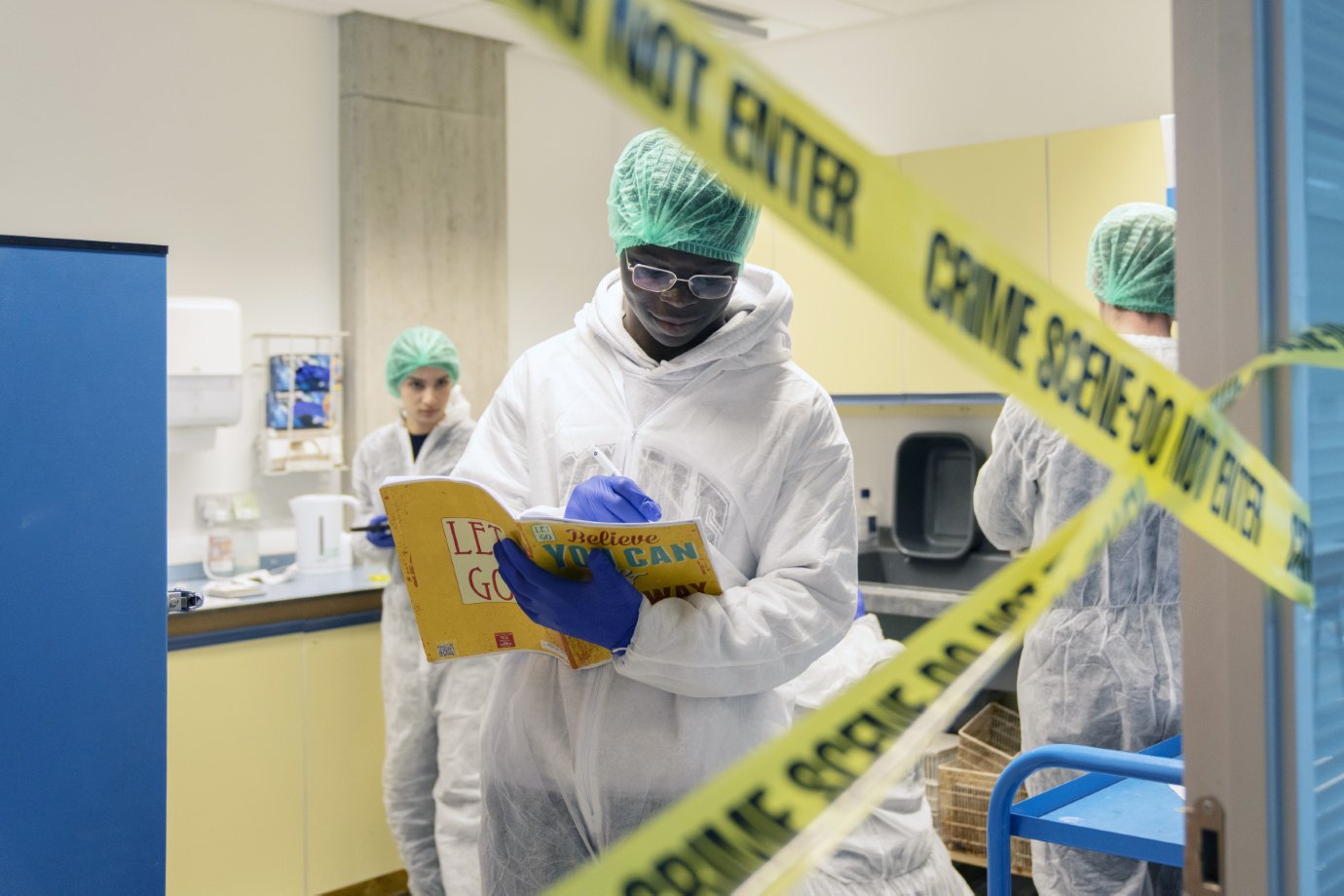 Forensic science student reads instructions behind crime scene tape during a practical lab exercise.
