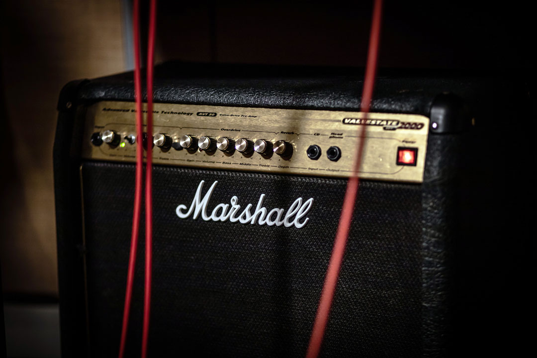 A close-up of a Marshall amplifier with red audio cables plugged in, glowing indicator light visible.