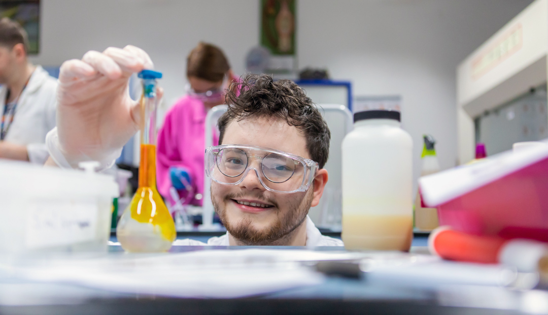 Science student smiling and holding a flask with yellow liquid in the laboratory at Glasgow Kelvin College