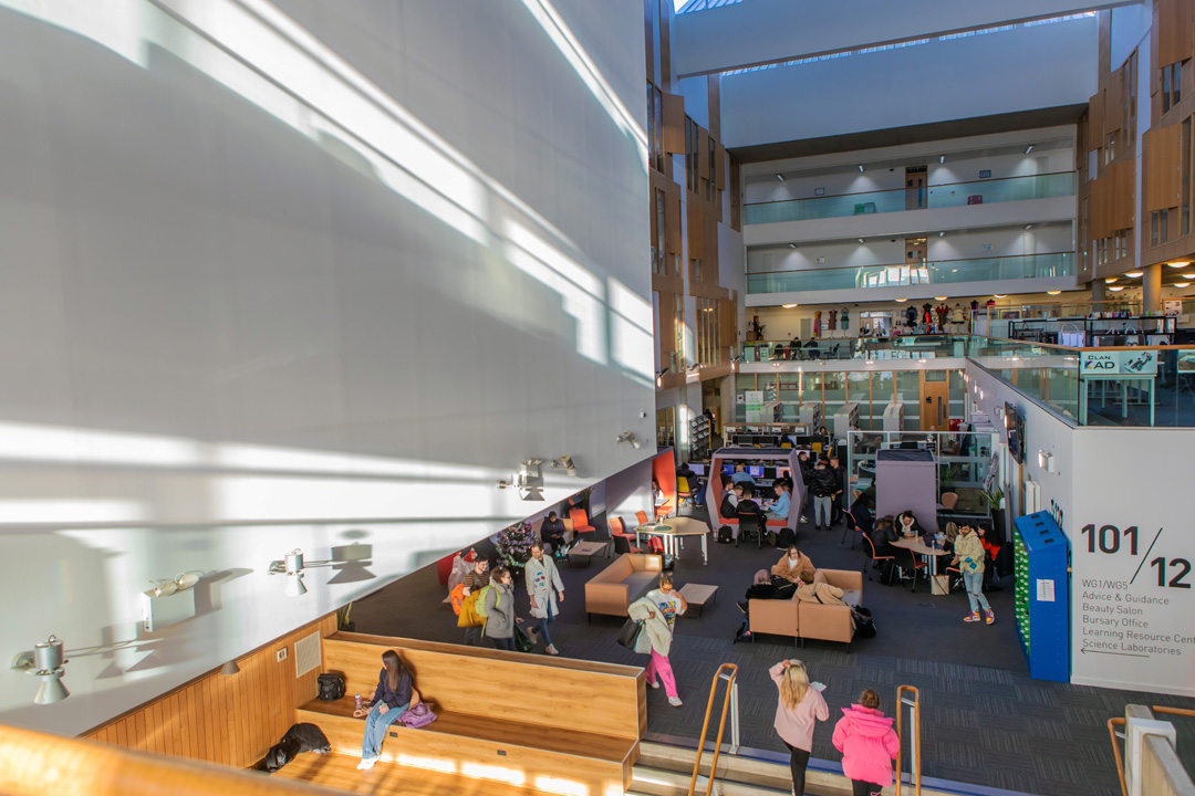 Bright, multi-level interior of Glasgow Kelvin College’s Springburn Campus, showing students studying and socialising in the central communal and library area.