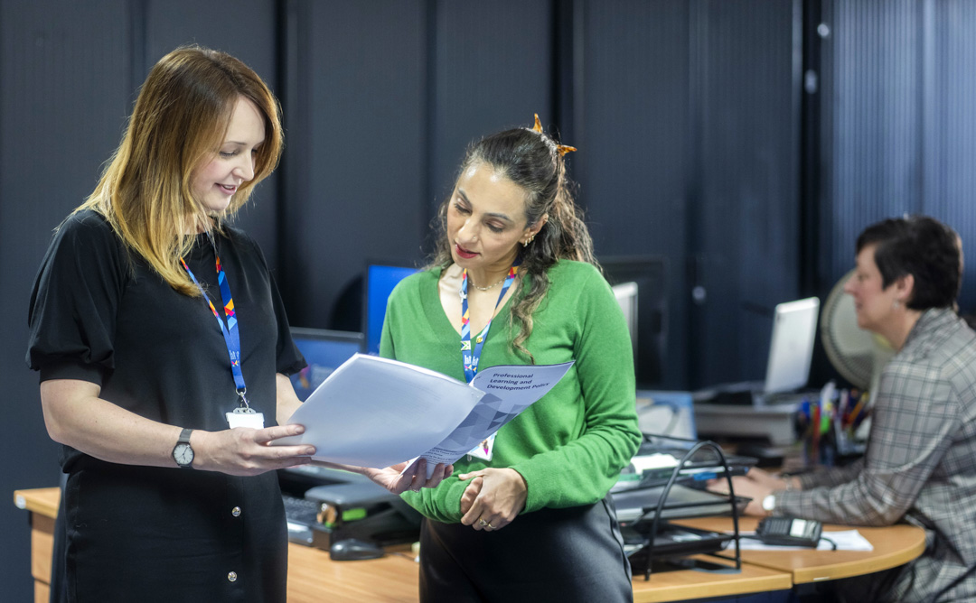 Two Glasgow Kelvin College staff members reviewing a document together at a desk, with a third colleague working at a computer in the background